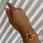 Brazalete dorado tipo argolla con broche circular — elegante y minimalista